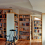 A home library with lots of built-in shelves, natural light, hardwood floors, recessed lighting, and two rocking chairs.