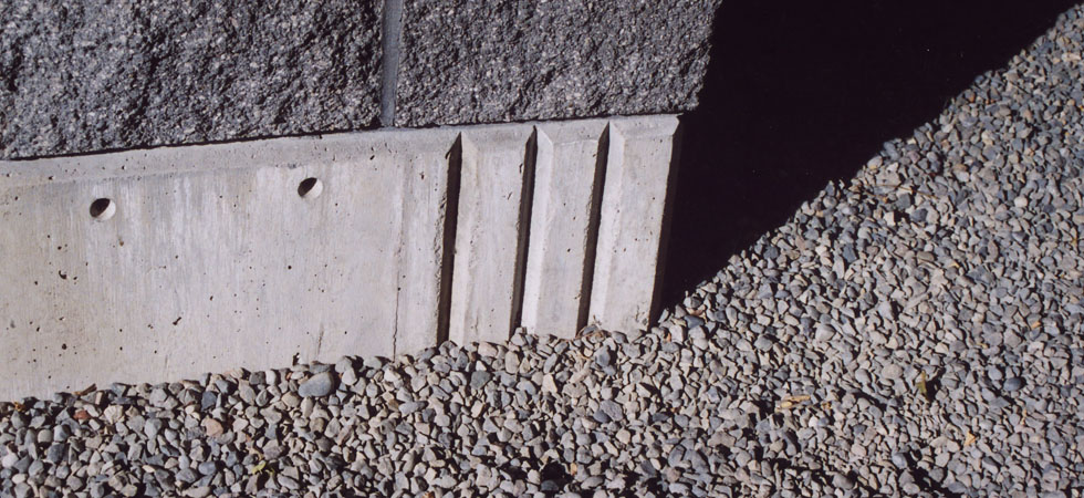 A close-up of the corner of a well-designed concrete foundation with a dark masonry block wall on top.